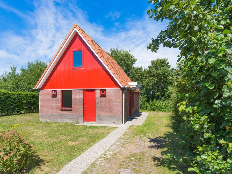 Typ II+ - Nr. 77 Goldfinch, Ferienhaus in Oosterend Texel mit roter Fassade und gruenem Garten.