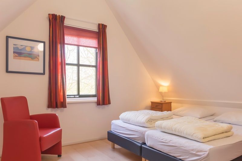 Comfortable bedroom with red chair in Type III - No. 21B Pheasant, Oosterend, Texel.
