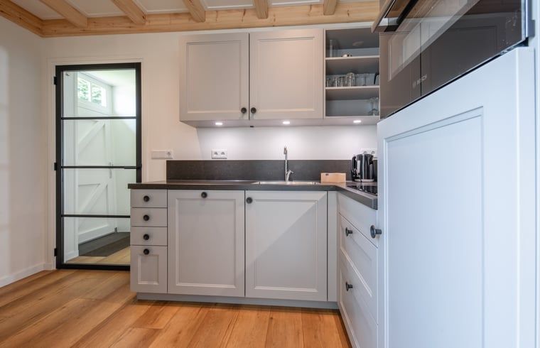 Moderne Kueche im Ferienhaus in Oudeschild, Texel, mit stilvollen Schraenken und Geraeten.