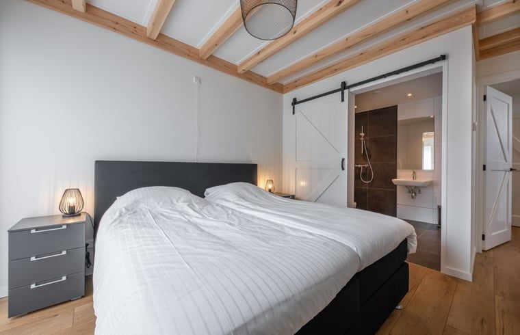 Schlafzimmer mit eigenem Bad in einem Ferienhaus in Oudeschild, Texel, mit Zugang zu einem modernen Badezimmer.