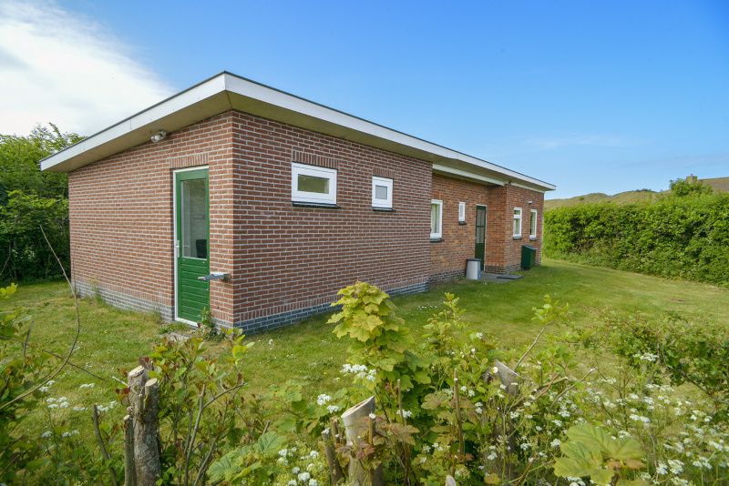 Zijaanzicht van Slufterbungalows 362 in Bungalowpark Slufteroord, Texel met groene omgeving en blauwe lucht.