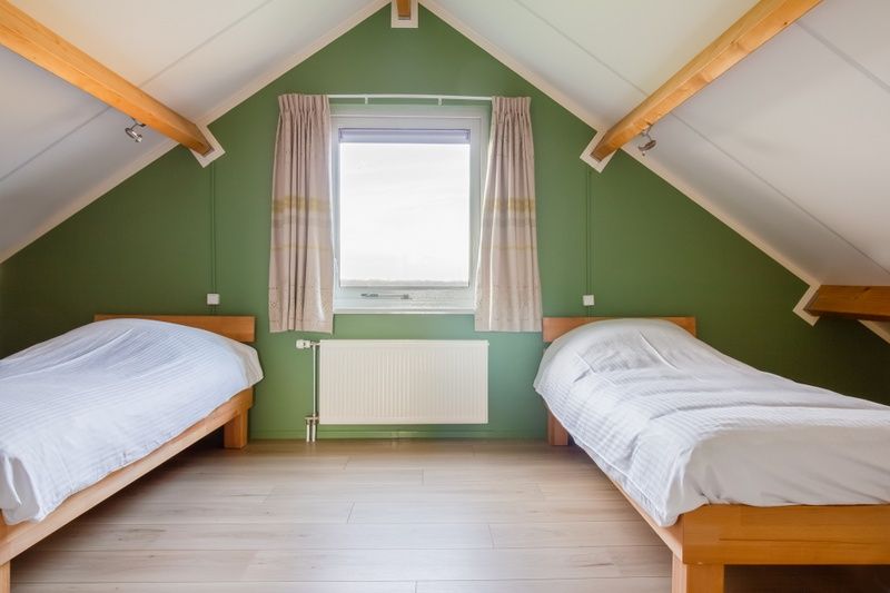 Cozy attic room in De Triaan vacation homes, South Eierland, Texel, with wooden beams and two beds.