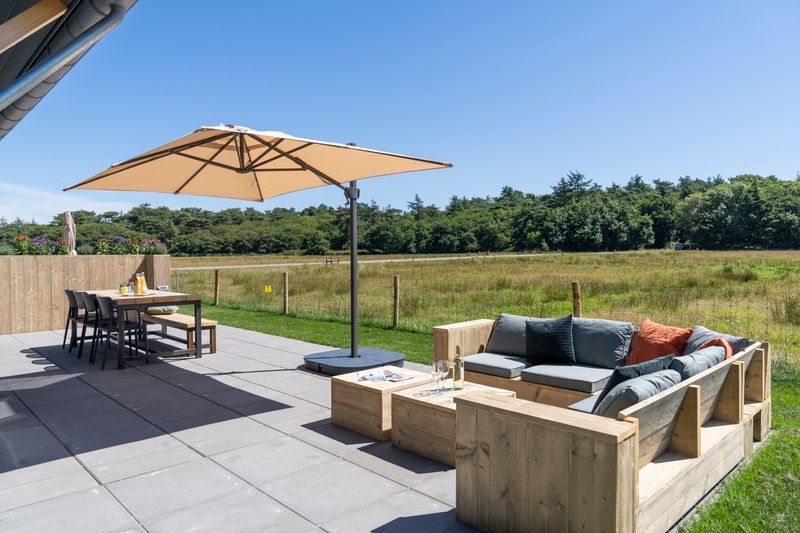 Spacious terrace of Holiday home 2 on Texel with parasol and wooden garden furniture.