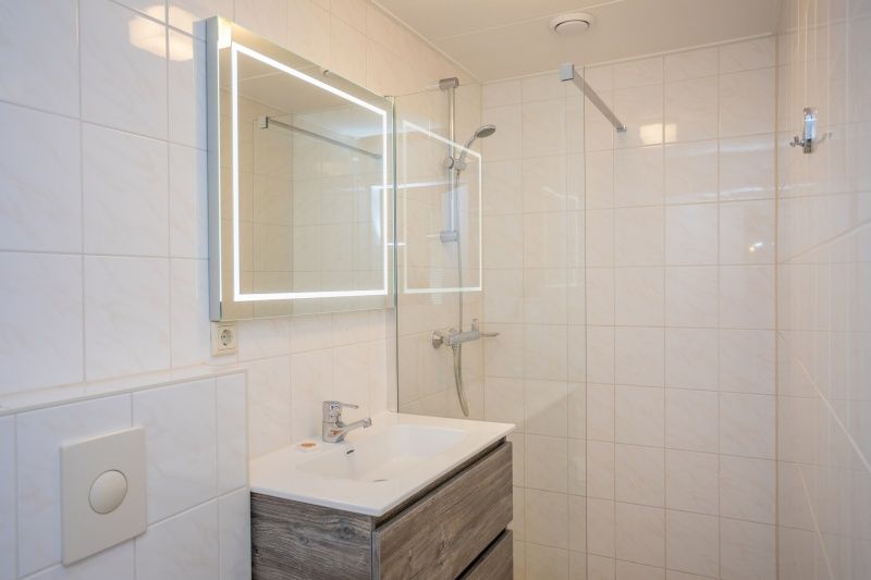 Moderne badkamer in Appartement Bos en Duin 30, De Dennen, Texel met inloopdouche en verlichte spiegel.