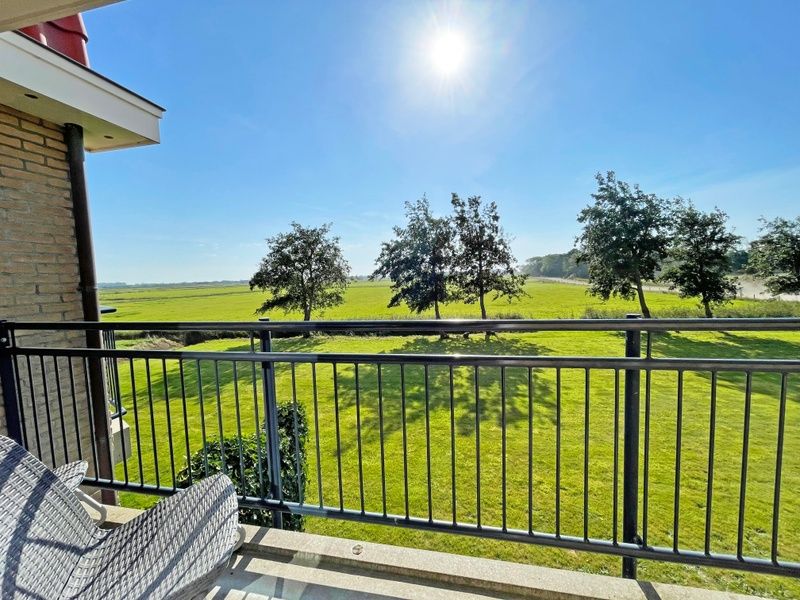 Uitzicht vanaf het balkon van Appartement Bos en Duin 42, Texel met weidse groene velden en stralende zon.