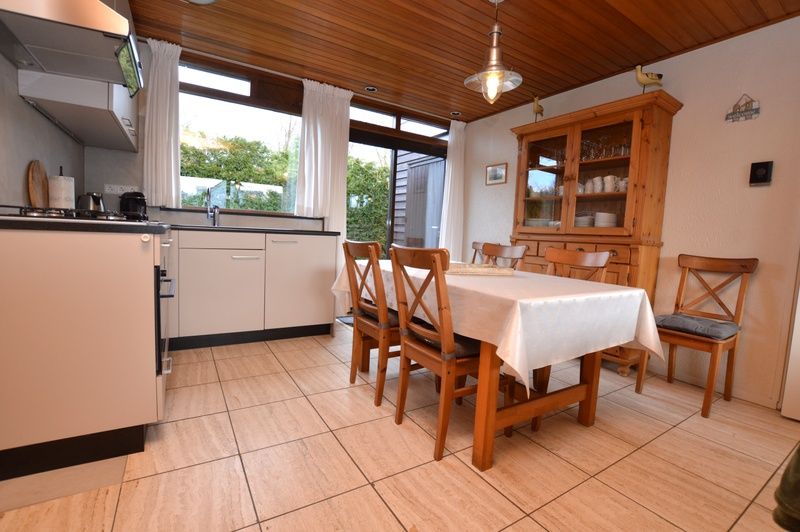 Dining area and kitchen in Holiday home de Parel 258, Texel, with wooden furniture and lots of light.