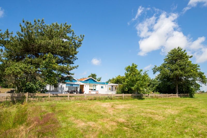 View of Weidezicht in De Dennen, Texel, surrounded by greenery and clear blue sky.