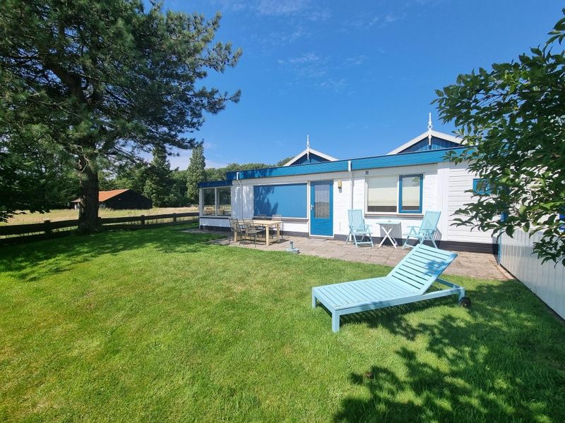 Veranda of Weidezicht vacation home in De Dennen, Texel with deck chairs and lawn.
