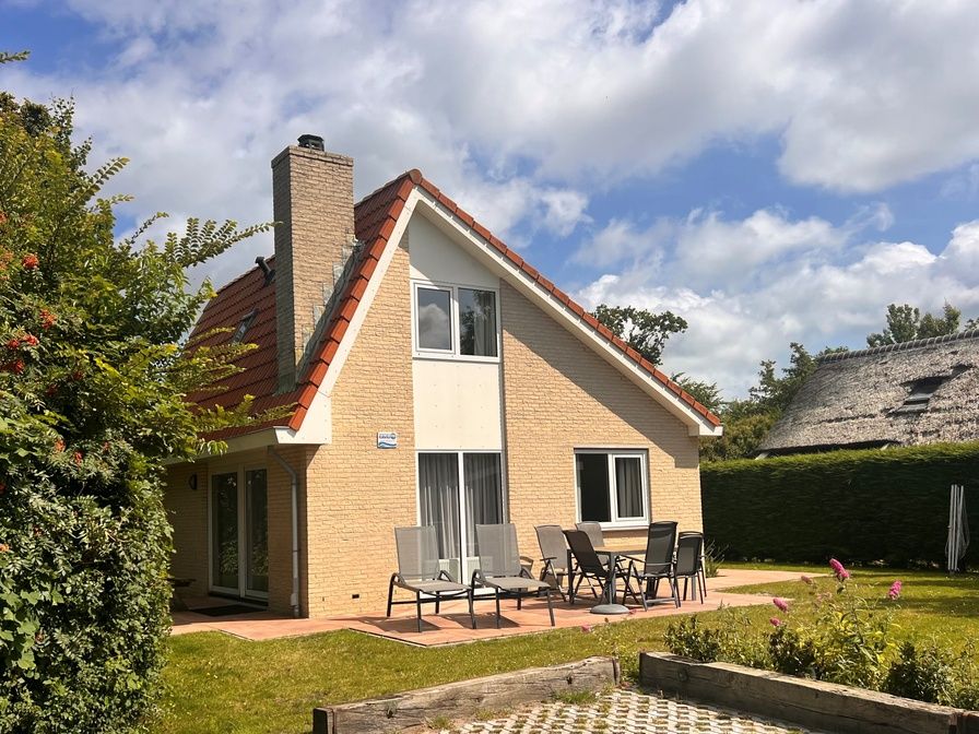 Aussenansicht des Ferienhauses 't Hoogelandt 136 in De Dennen, Texel, mit sonniger Terrasse und gruener Umgebung.