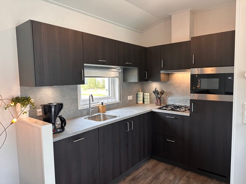 Modern kitchen in Holiday Park de Bremakker - Bosveld 141, Texel with dark wood cabinets and complete equipment.