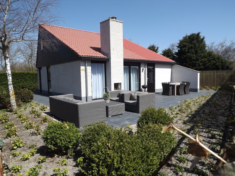 Buitenzijde van Vakantiehuis Gortersmient 320, De Dennen, Texel met comfortabele zithoek en eettafel op het terras, perfect voor buitenleven.