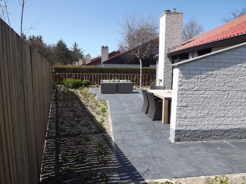 Ruim terras van Vakantiehuis Gortersmient 320, De Dennen, Texel met moderne tuintafel en stoelen, omgeven door natuurlijke omgeving.