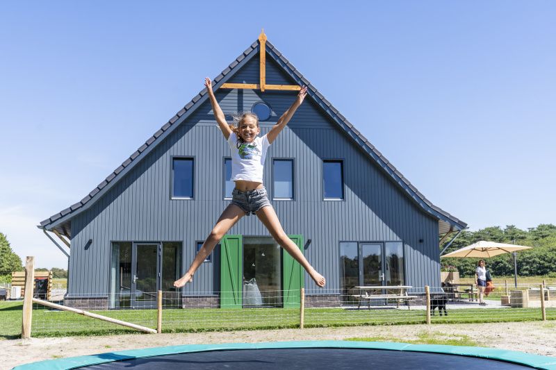 Kinderspass auf dem Trampolin im Ferienhaus 1 in De Dennen Texel, mit dem Ferienhaus im Hintergrund.