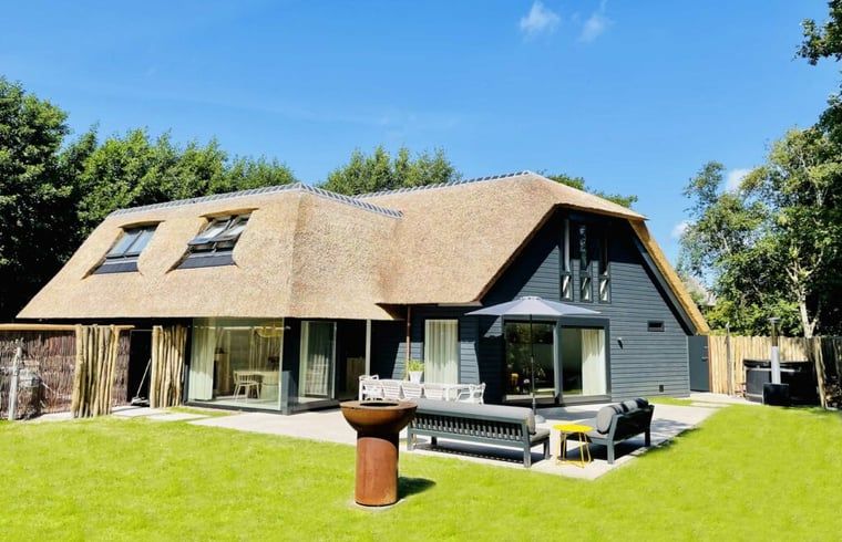 Charmant vakantiehuisje in Ballum met rieten dak, Ameland, omgeven door groen.