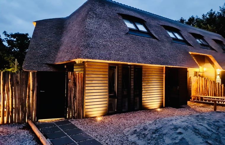 Verlichte buitenkant van vakantiehuisje in Ballum, Ameland bij schemering.