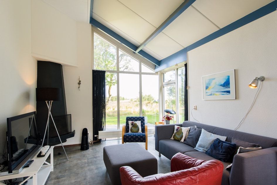 Ruime woonkamer in Duinvilla 6, een bungalow in Hollum, Ameland, met grote ramen en uitzicht op de natuurlijke omgeving van de Waddeneilanden.