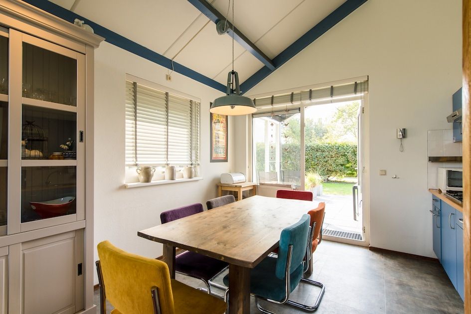 Gezellige eetkamer in Duinvilla 6, een bungalow in Hollum op Ameland, met een rustgevend uitzicht op de tuin en kleurrijke stoelen rondom de tafel.