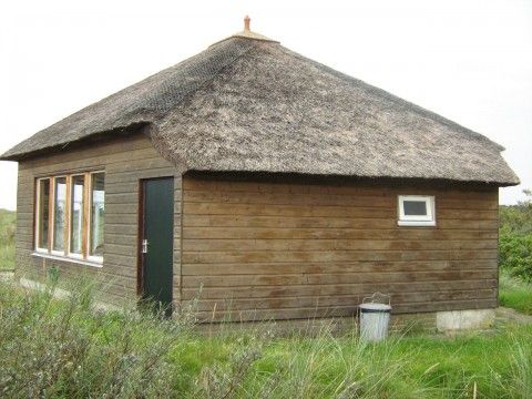 Buitenzijde van houten vakantiehuis De Vijfhoek in Nes, Ameland met rieten dak.