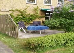 Genieen Sie die sonnige Veranda des Ferienhauses Kia-Ora auf Schiermonnikoog mit bequemen Sitzgelegenheiten und grner Umgebung.