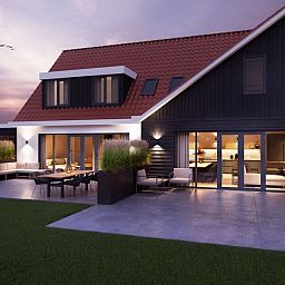 Illuminated evening view of 6 person vacation home in De Cocksdorp Texel with terrace.