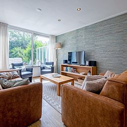 Gemuetliches Wohnzimmer im Ferienhaus Slufterhoek 132, De Cocksdorp, Texel, mit bequemen Sofas und Blick auf den Garten