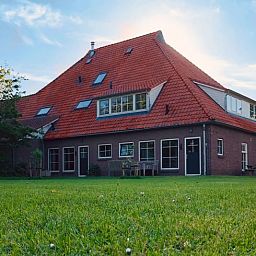 Hinterer Garten und Terrasse des Ferienhauses in De Cocksdorp, Texel, mit grossen Rasenflaechen.