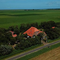 Luftaufnahme des Ferienhauses in De Cocksdorp, Texel, umgeben von gruenen Feldern und natuerlicher Schoenheit auf den Waddeninseln.