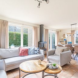 Bright living room of vacation home Honeysuckle 81 in De Koog, Texel with comfortable seating area and garden view, ideal for relaxation.