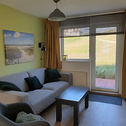 Sunny sitting area in De Duinpan - Duinhuisje Texel, De Koog, overlooking the dunes through large windows.