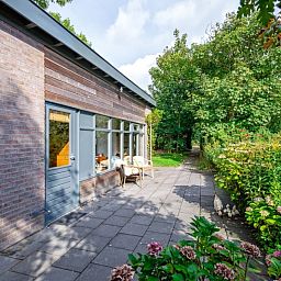Aussenbereich des Ferienhauses De Zonneweelde in De Koog, Texel, mit bluehenden Pflanzen und sonniger Terrasse.