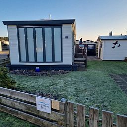 Chalet Bregkoog 33 in Chaletpark Bregkoog, De Koog, Texel, offers a serene outdoor space with a manicured lawn and wooden fence.