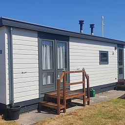 Sunny exterior of Chalet Bregkoog 33, Chaletpark Bregkoog, De Koog, Texel, with an inviting terrace and wooden steps.