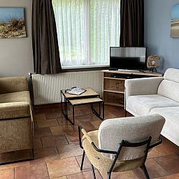 Cozy living room of Koetshuis vacation home in De Koog, Texel, with comfortable sofas and a television for relaxation.
