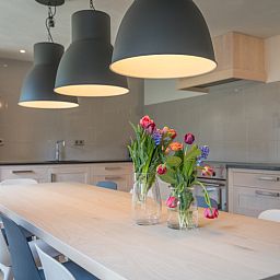 Gemuetlicher Essbereich im Ferienhaus Orchismient 24, De Koog, Texel, mit Blumen auf dem Tisch und Haengelampen.