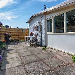 Private Terrasse Ferienhaus 2490, De Koog, Texel, mit Holzzaun und bunten Blumen.