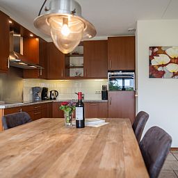 Dining area and kitchen of Villa 304 in De Koog, Texel with stylish wooden table for cozy meals.