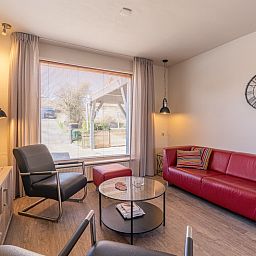 Gemuetliches Wohnzimmer in De Zandduyn, De Koog, Texel, mit rotem Sofa und grossen Fenstern fuer natuerliches Licht.