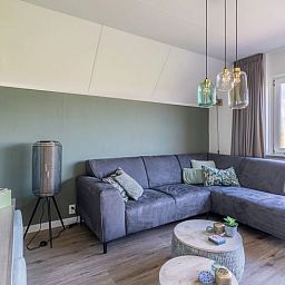 Gemuetliches Wohnzimmer im Ferienhaus in De Waal, Texel mit bequemem Ecksofa und Blick auf die gruene Umgebung.