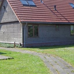 Seitenansicht des Ferienhauses Duinzicht in Den Burg Texel mit roten Dachziegeln und Rasen.