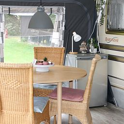 Essecke im Caravan Rust & Ruimte, Den Hoorn, Texel, mit Holztisch und Korbstuehlen fuer eine gemuetliche Atmosphaere.
