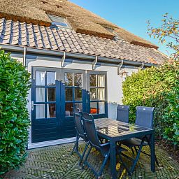 Terrasse des Ferienhauses in Oosterend, Texel, Ferienhaus mit Tisch im Freien, umgeben von Gruen auf den Watteninseln.