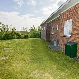 Achtertuin van vakantiehuis Slufterbungalows 362 in Bungalowpark Slufteroord, Texel omgeven door weelderige natuur.