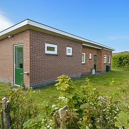 Zijaanzicht van Slufterbungalows 362 in Bungalowpark Slufteroord, Texel met groene omgeving en blauwe lucht.