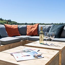 Cozy sitting area on the terrace of Holiday Home 2 in De Dennen, Texel with cushions and wine.