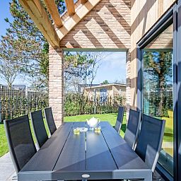 Bungalowpark 't Luwe Land - Nieuw Vredelust, De Dennen, Texel. Gezellige eethoek op het terras met uitzicht op de groene tuin.