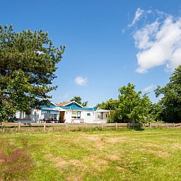View of Weidezicht in De Dennen, Texel, surrounded by greenery and clear blue sky.