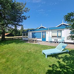 Veranda of Weidezicht vacation home in De Dennen, Texel with deck chairs and lawn.