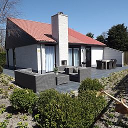 Buitenzijde van Vakantiehuis Gortersmient 320, De Dennen, Texel met comfortabele zithoek en eettafel op het terras, perfect voor buitenleven.