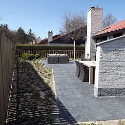 Ruim terras van Vakantiehuis Gortersmient 320, De Dennen, Texel met moderne tuintafel en stoelen, omgeven door natuurlijke omgeving.