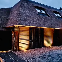 Verlichte buitenkant van vakantiehuisje in Ballum, Ameland bij schemering.